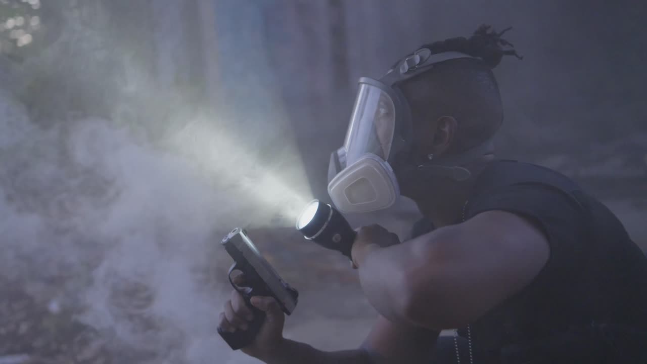 A man in a gas mask scans a smoky, abandoned area with a flashlight while holding a pistol. Suspenseful, cinematic action vibe