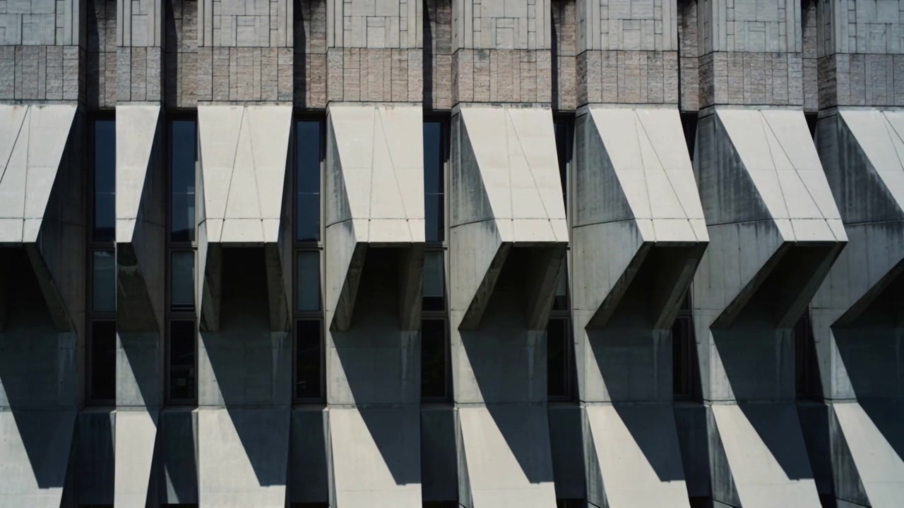 Shifting sun moving shadows across concrete windows with angled sunshades at street, low sun angle