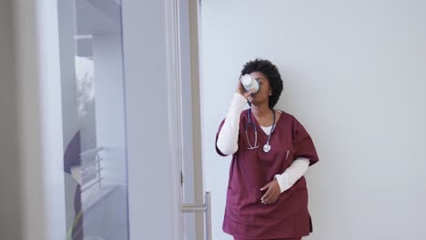 tired african american female doctor drinking coffee in hospital, slow motion