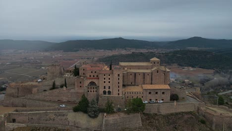 Historic-Cardona-Castle-and-town-under-a-cloudy-sky,-surrounded-by-mountains-and-greenery