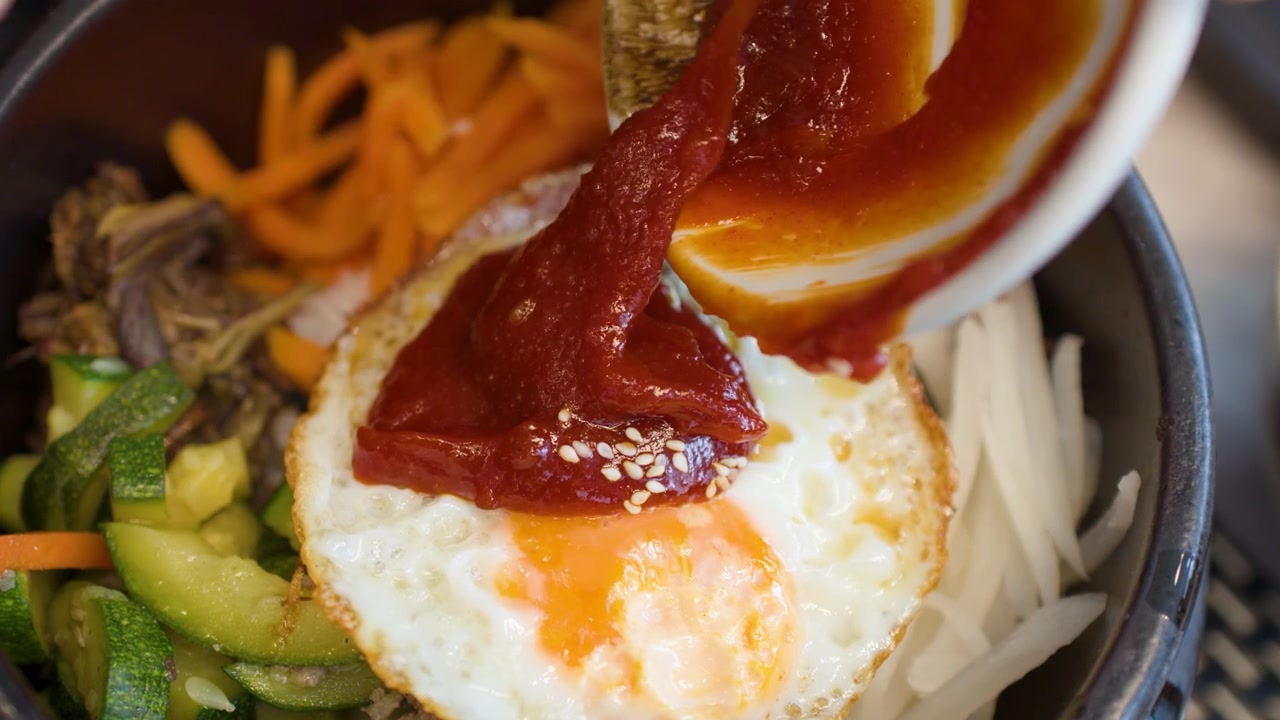 Pasta cabai merah dituangkan ke atas telur goreng dalam mangkuk bibimbap tradisional Korea.