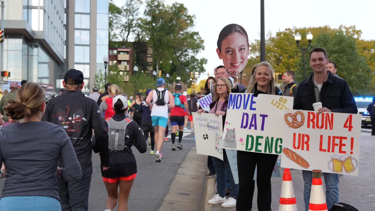Cheerful spectators holding funny signs cheer for runners during a marathon race
