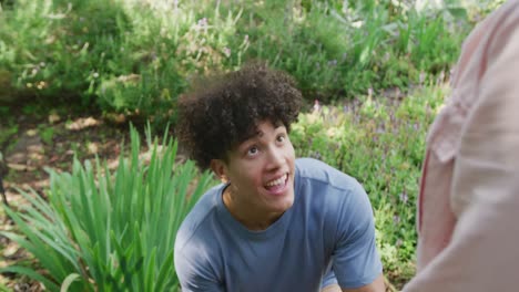 Happy-diverse-couple-proposing-and-smiling-in-garden-on-sunny-day