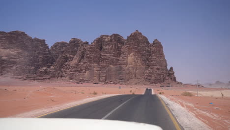 conduciendo en el desierto por una carretera asfaltada con vistas al acantilado de arenisca y al paisaje seco en un día caluroso y soleado, punto de vista del pasajero, wadi rum jordan