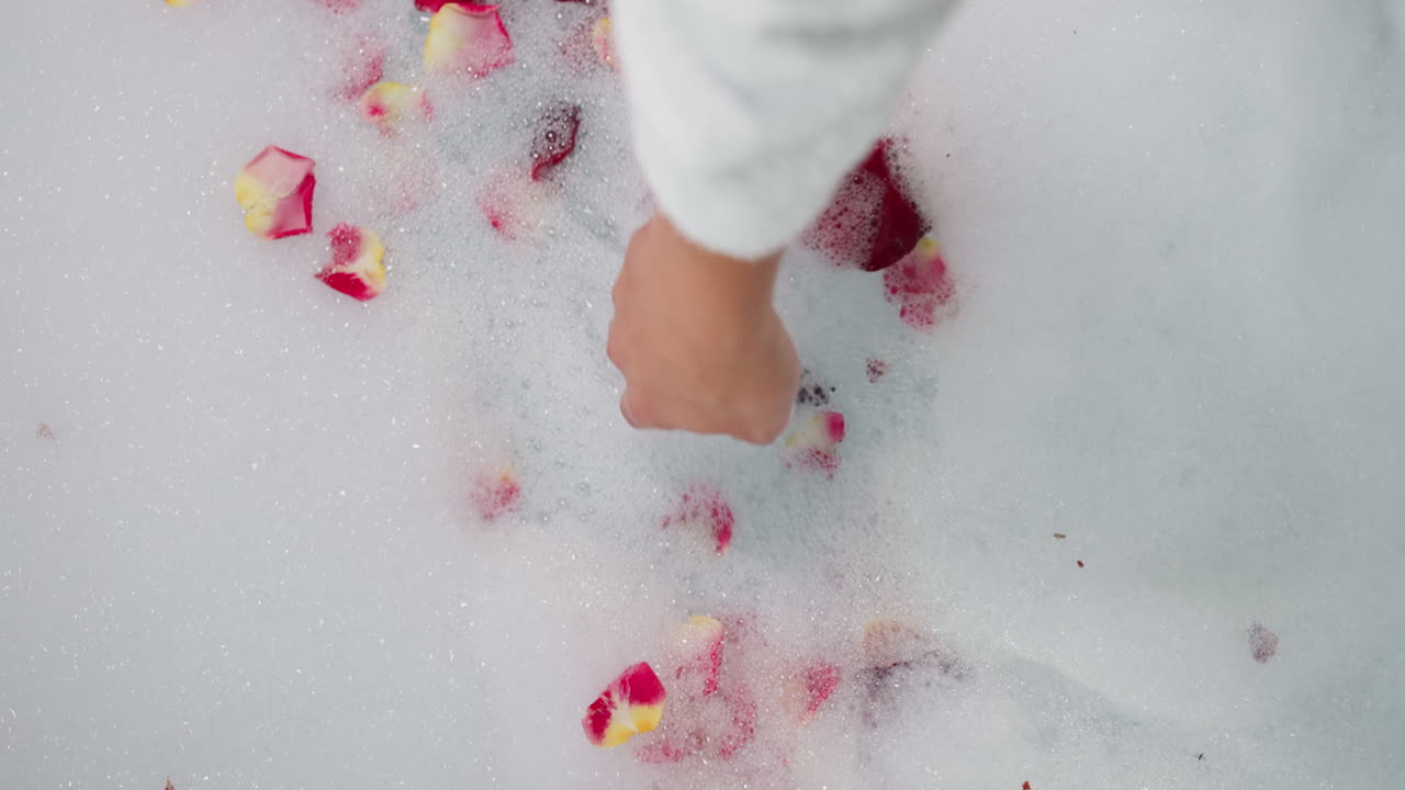 Woman touches foam with rose petals closeup. Lady prepares relaxation procedure in romantic atmosphere to celebrate Valentine day. Celebration idea