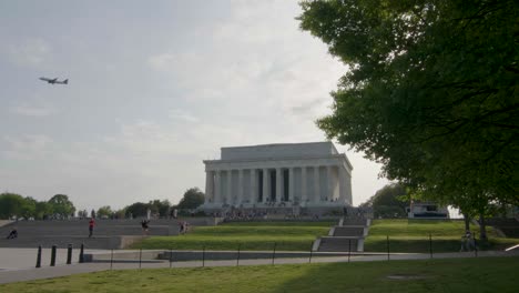 the lincoln memorial stands on a sunny spring day as a plane flies overhead and pedestrians enjoy the surroundings