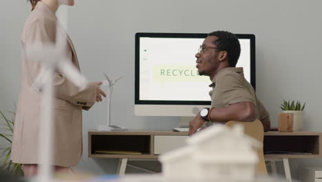 woman explaining something about a project to her colleague who is sitting at desk 1