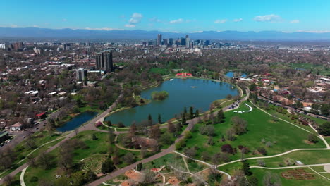 leo city park denver colorado lake pavilion vibrant spring summer aerial drone front range cityscape green lush grass trees blossom sunny blue sky snow capped rocky mountains circle left motion