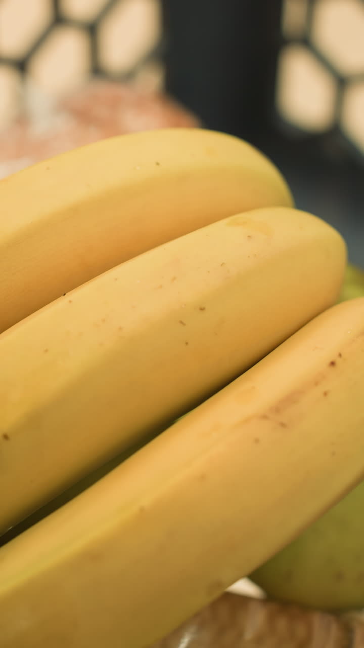 vista de cerca de una mano colocando plátanos en un carrito de compras que ya contiene un paquete de galletas, un pan y varias manzanas