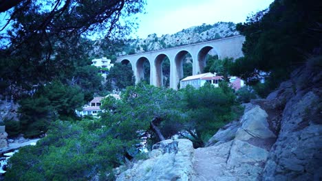 Wunderschöne-Eisenbahnbrücke-über-Ein-Kleines-Tal-In-Frankreich-Zwischen-Felsen-Und-Natur-Mit-Einem-Kleinen,-Ruhigen-Haus-Dazwischen-In-Der-Sonne