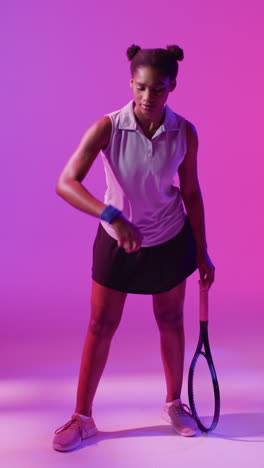 video vertical de una jugadora de tenis afroamericana rebotando la pelota en el relámpago rosa de neón