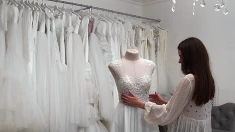 hermosa niña buscando vestido de novia en la cabina en comparación con otros vestidos. preparando para la boda. comprando un vestido de novia. la costurera inspecciona el vestido de novia hecho a medida terminado.