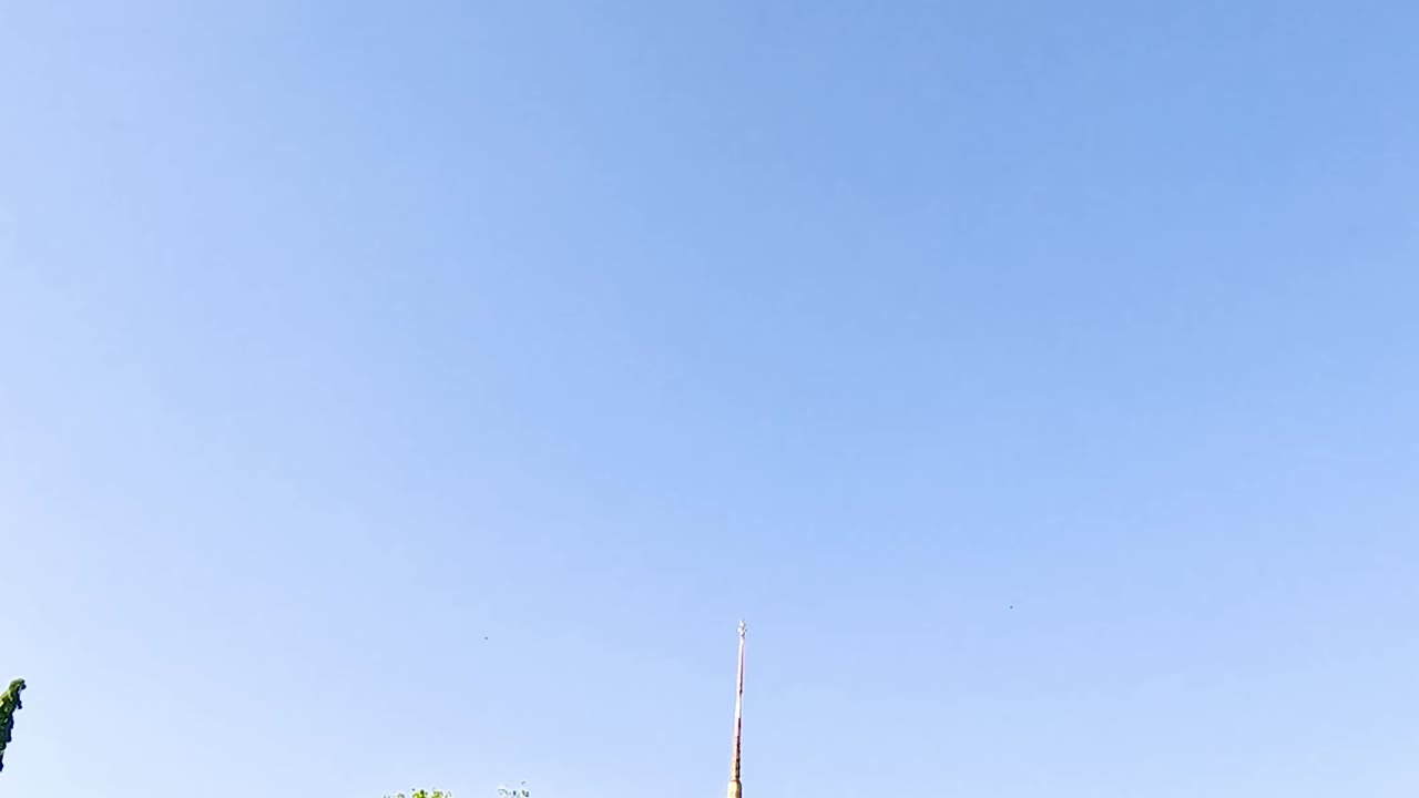 A traditional Thai pavilion stands gracefully by a serene lake, surrounded by lush greenery and a clear blue sky.