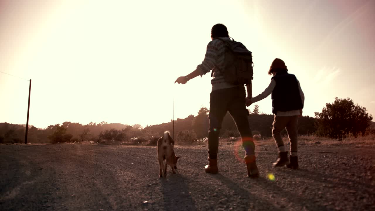 padre y hijo jóvenes caminando por el sendero de la montaña con el perro