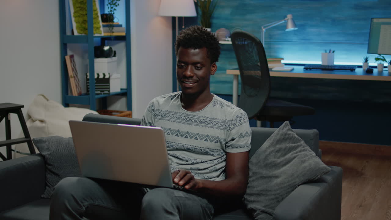 African american freelancer using laptop for remote work while sitting on couch