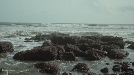 Waves-crash-against-jagged-rocks-on-a-cloudy-day