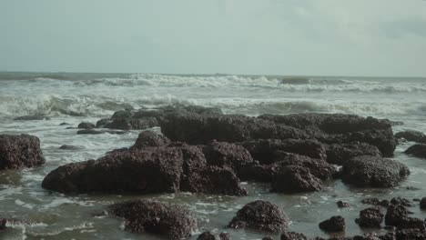waves crash against jagged rocks on a cloudy day