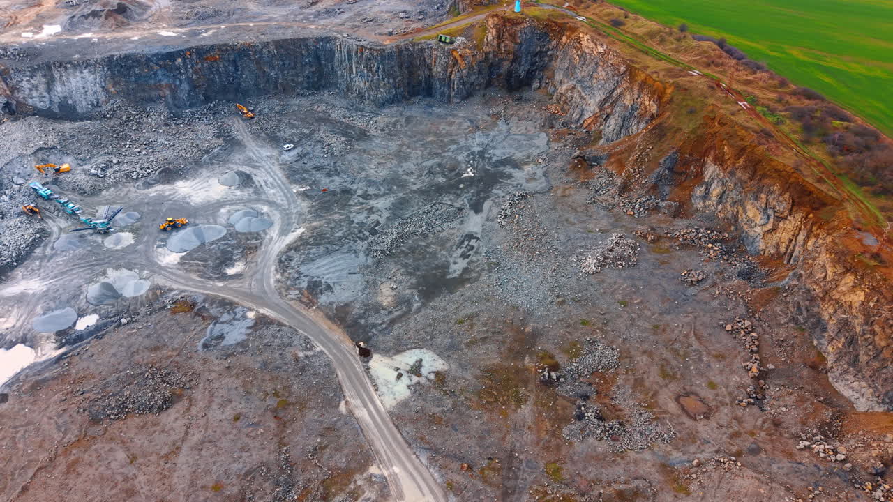 Granite quarry wall with gravel piles and industrial machinery. High angle view of a steep rock face and sorting equipment in an open pit mine