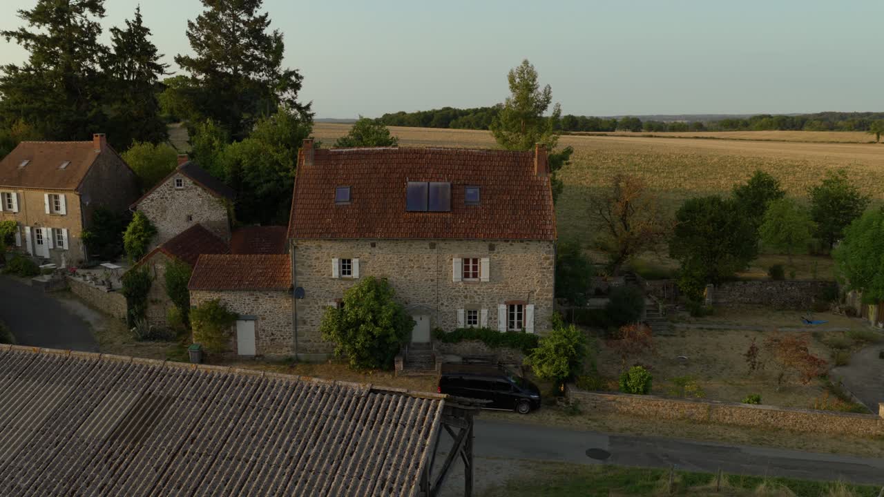 Aerial view of a countryside village with stone houses, barns, and winding roads glowing in warm sunset light