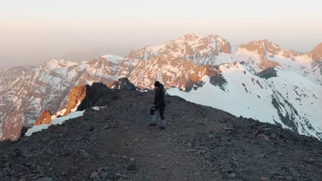 Joven-Caucásica-Vestida-De-Invierno-Caminando-Por-Una-Montaña-Durante-El-Amanecer-En-El-Alto-Atlas,-Monte-Toubkal,-Marruecos