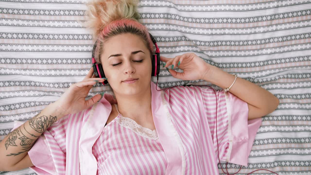 retrato de una hermosa joven de cabello rosa acostada en la cama y escuchando música con auriculares