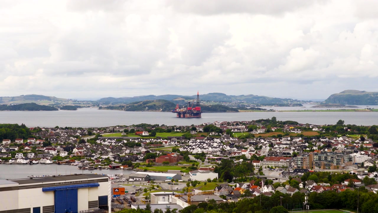 Aerial view, Stavanger, Norway, showing an offshore heavy lift crane vessel in the fjord beyond a coastal urban area, highlighting marine engineering and offshore industry