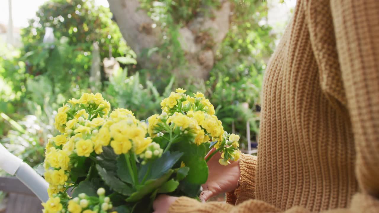 mujer caucásica sonriente trasplantando flores amarillas en un jardín soleado