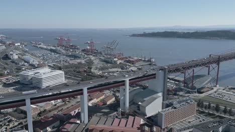 Panning-shot-of-the-25-de-Abril-Bridge-with-Alcantara-docks-and-tagus-river-in-background-in-Lisbon,-Portugal