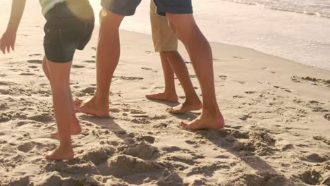 Mid-section-of-man-with-children-walking-on-the-sand