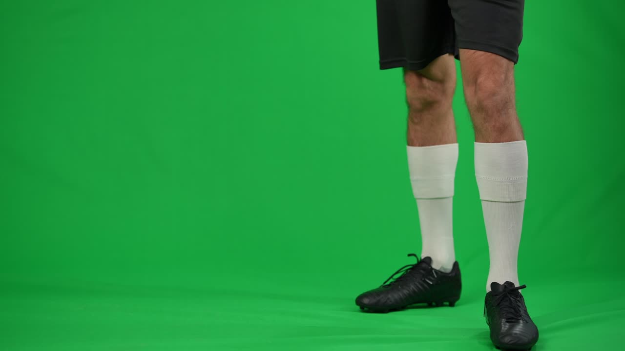 Giovane sportivo che salta e passa un pallone da calcio su sfondo in chromakey. Uomo caucasico irriconoscibile che esegue un trucco calcistico su schermo verde. Concetto di abilità e sport.