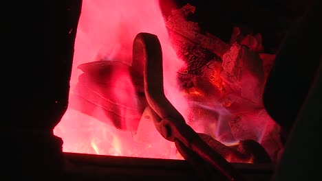 blacksmith moving stacked metal bowls with tongs over hot flames in ancient traditional oven, over shoulder