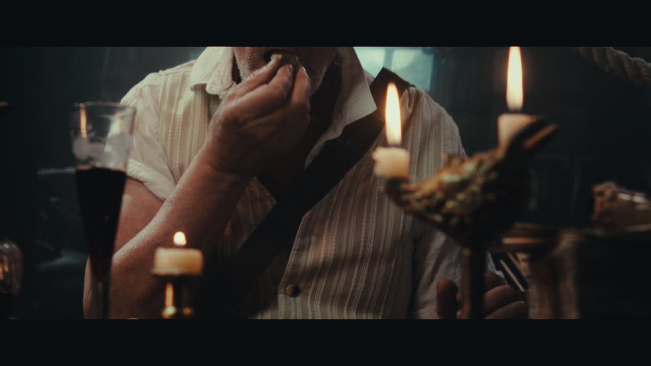 An old pirate eats and drinks inside the sailing ship cabin