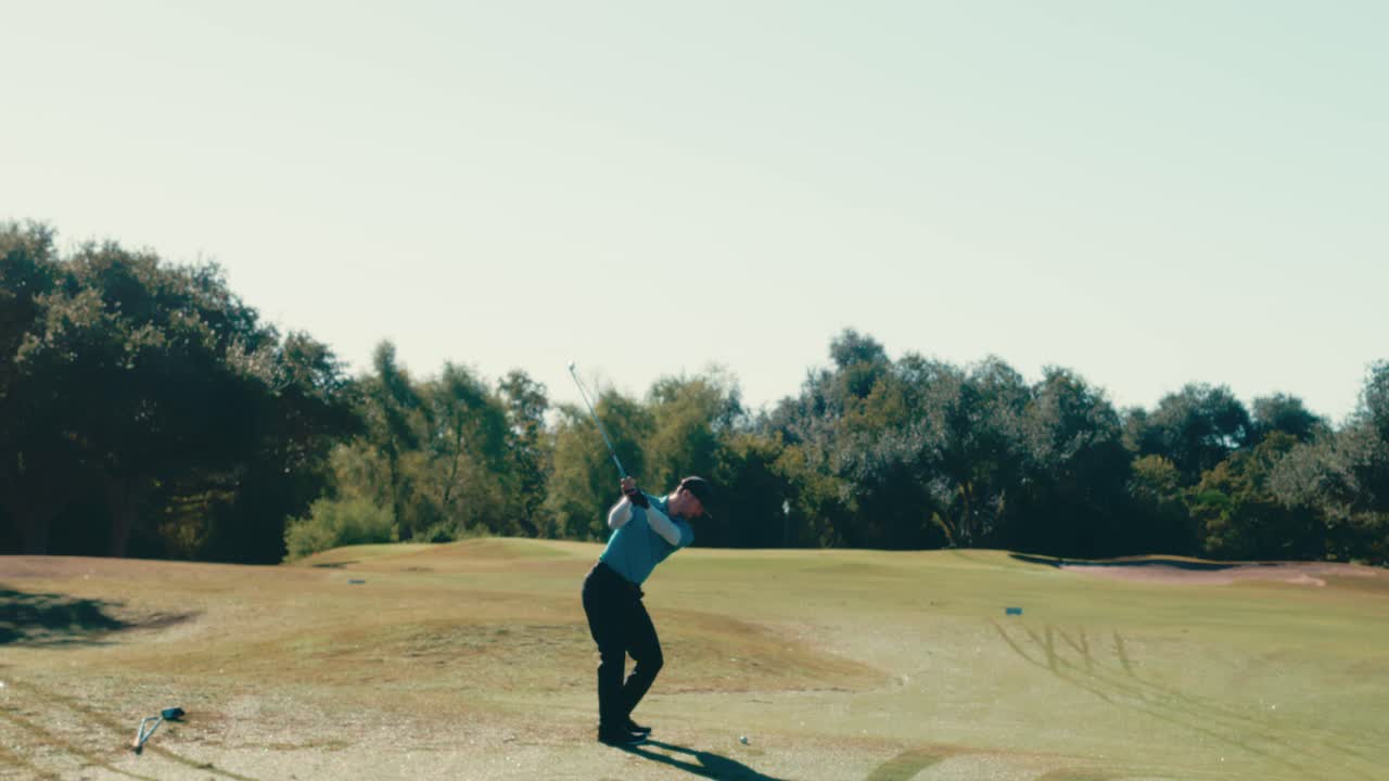 Male golfer hits an iron from behind in slow motion, sending the ball toward the flag with the pin visible in the distance