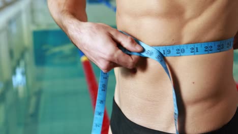 close up mid section of a shirtless fit swimmer measuring waist