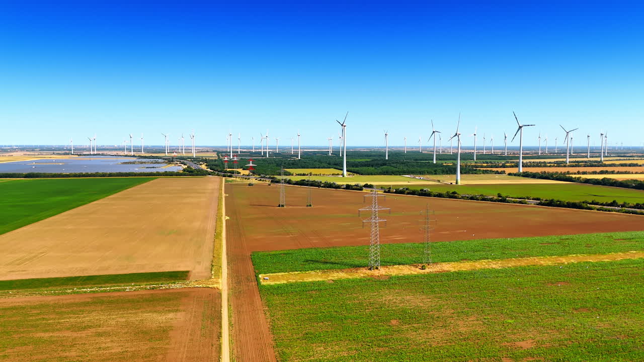 Rising over the fields in the rural area. Electricity power lines, solar panels and wind turbines located in the countryside. Aerial view