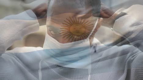 Animation-of-flag-of-argentina-waving-over-african-american-man-wearing-face-mask-in-city-street