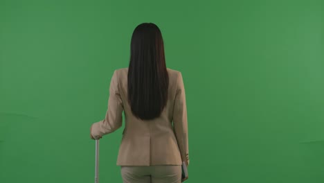 vista trasera mujer de negocios asiática viajera con equipaje caminando y de pie en el estudio de fondo de pantalla verde, durante la hora de la puesta del sol