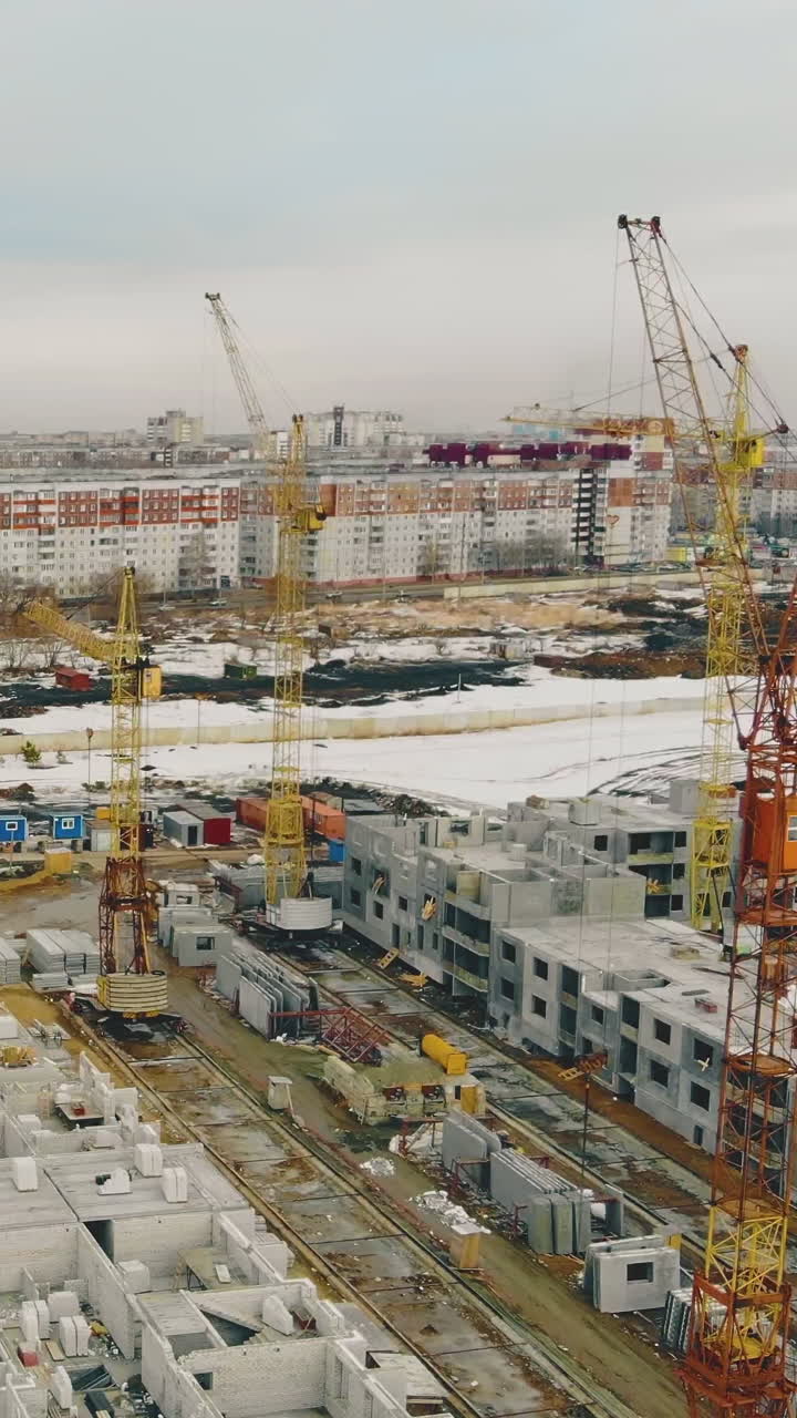 large construction site with building in progress and yellow cranes on weekend against distant city on cloudy day aerial