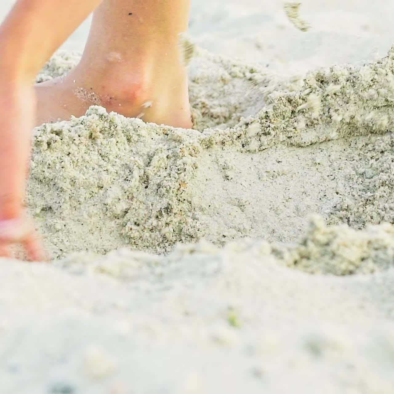 A kid gets up in a sandy pit with his legs to measure it and continues to expand its length and width. Close-up.