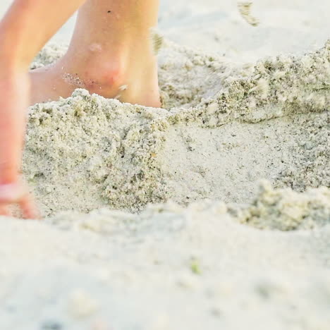 a kid gets up in a sandy pit with his legs to measure it and continues to expand its length and width. close-up.