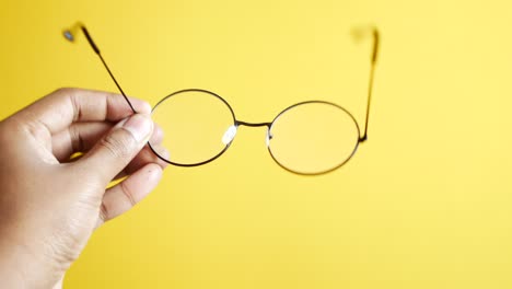 mano con gafas redondas contra un fondo amarillo