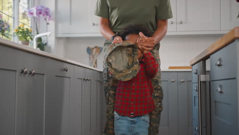 american army mother in uniform home on leave playing with son in family kitchen