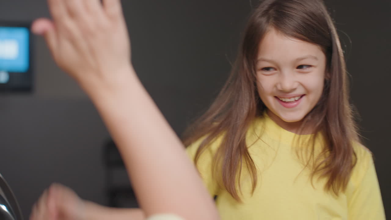 Close view of girl in yellow swinging cloth, tossing fabric aside, sharing high five with seated adult in laundromat, blur background, playful team mood during loading process, candid moment