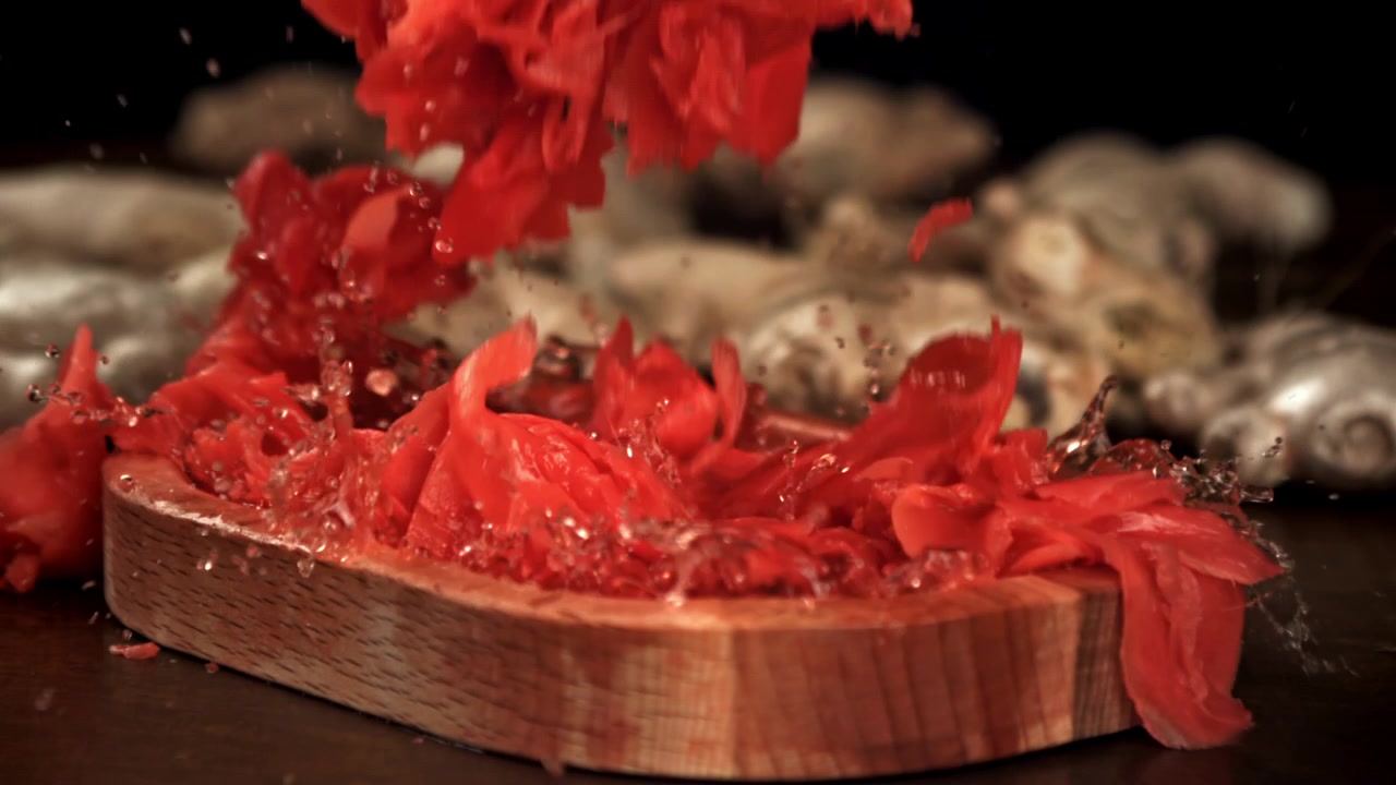 Zenzero rosso marinato che cade in una ciotola di legno al rallentatore.