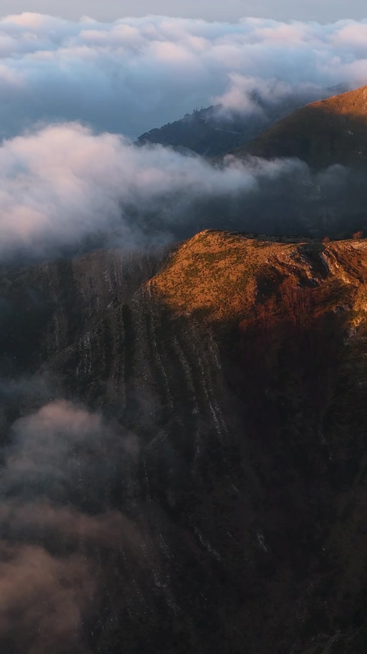Golden sunlight illuminates rugged Alpine peaks as dense clouds drift below at dusk