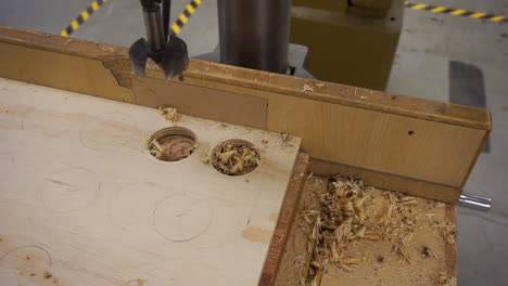 close up clip of a hand sweeping away wood shavings after drilling a hole in plywood with a drill press