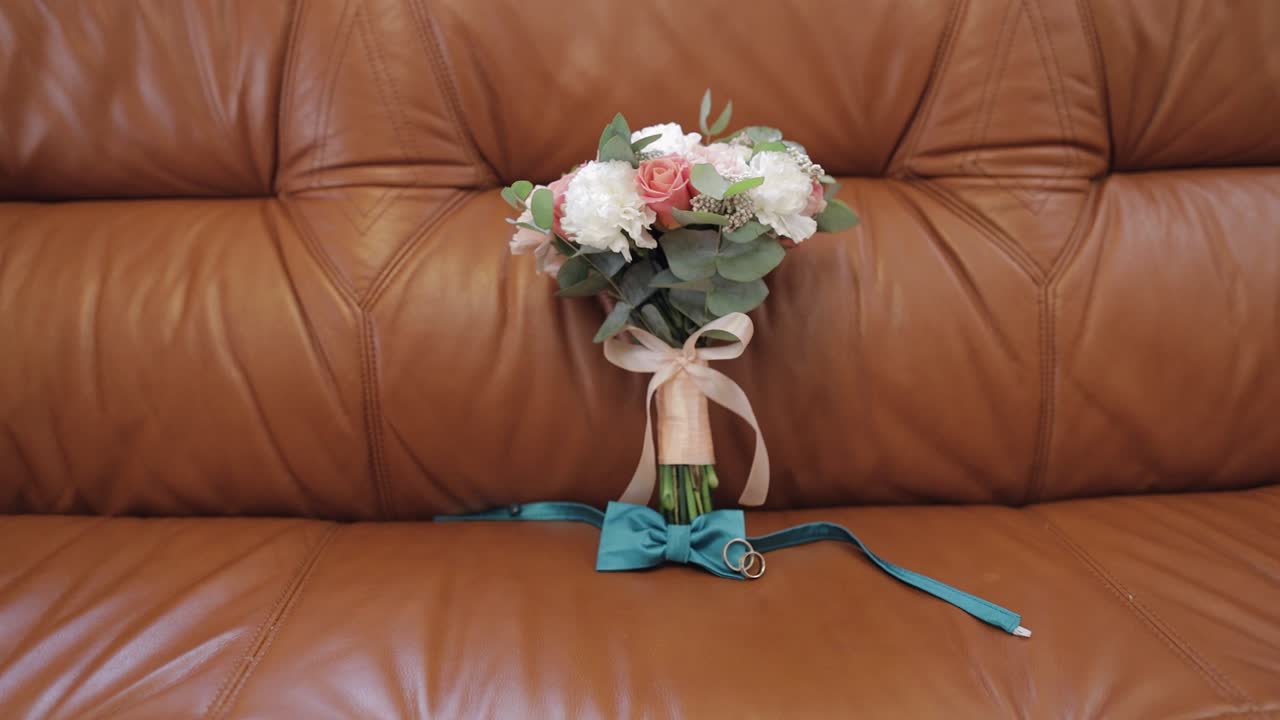 Bellissimi bouquet da sposa posati con anelli nuziali e il papillon dello sposo sul divano.