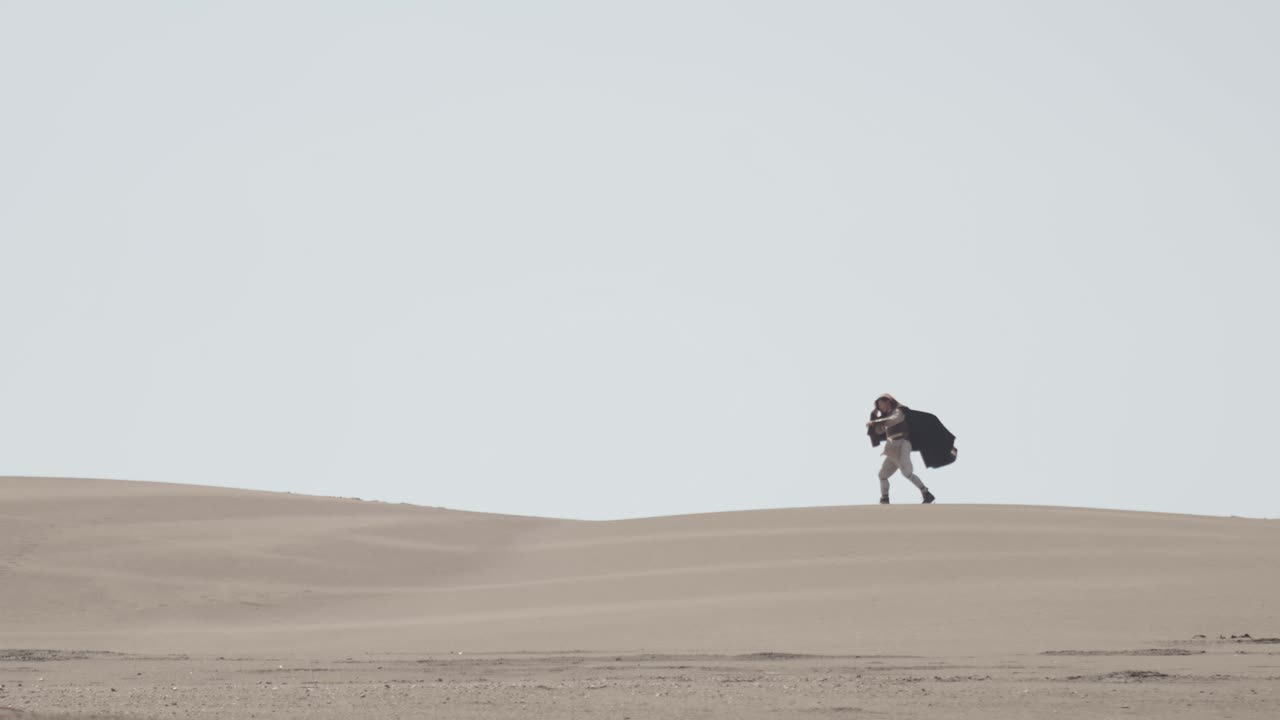 A robed figure struggles across a vast sand dune, then falls to their knees in exhaustion. Post-apocalyptic, sci-fi, or fantasy concept of despair, struggle, and survival