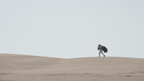 a robed figure struggles across a vast sand dune, then falls to their knees in exhaustion. post-apocalyptic, sci-fi, or fantasy concept of despair, struggle, and survival