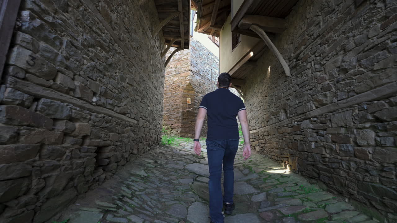 Young Man Walking Along The Ancient Homes In The Kovachevitsa Village In Garmen, Blagoevgrad Province, Bulgaria. - follow shot